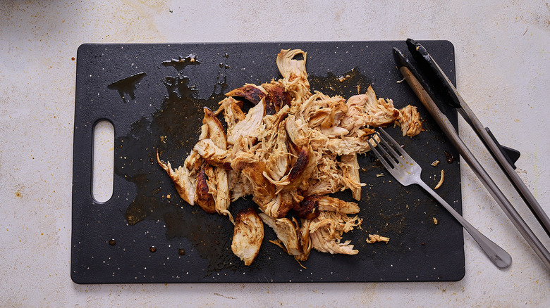shredding chicken on a cutting board
