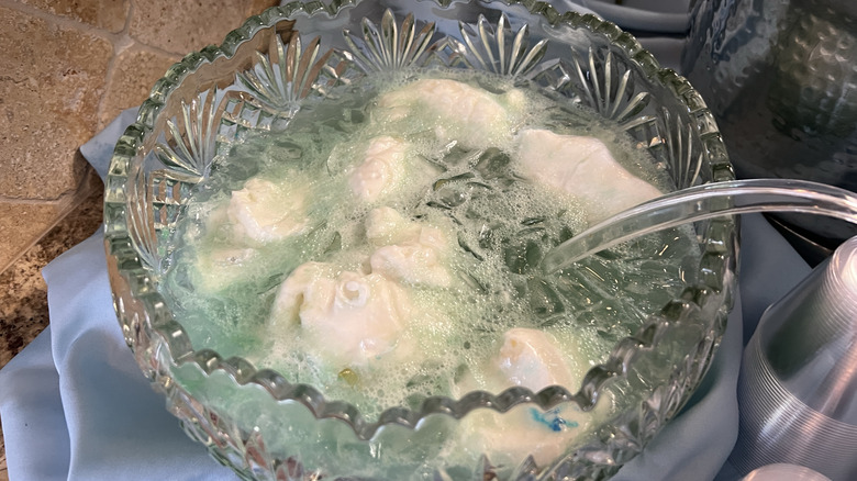 A large crystal bowl of blue punch with dollops of sherbet floating in it and a clear ladle resting in the bowl