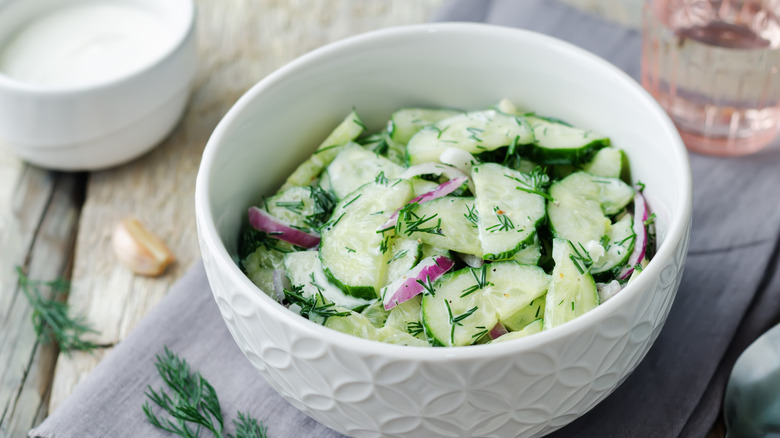 Cucumber and red onion salad in a white porcelain bowl with fresh dill garnish