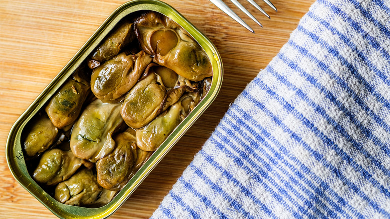open can of wood-smoked oysters on wooden table.
