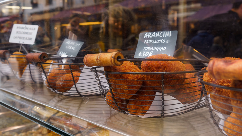 Baskets on different kinds of arancini in metal baskets sitting on a glass shop counter.