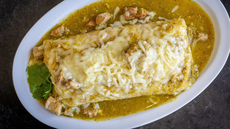 A burrito on a plate smothered with cheese and chile verde