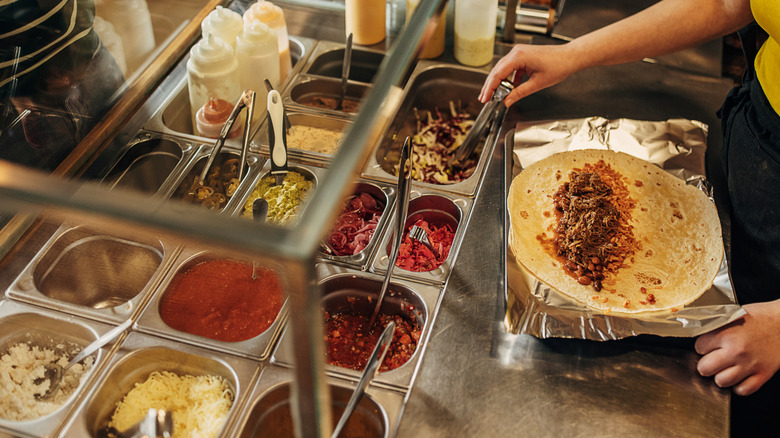 An employee builds a burrito for a customer from a bar of ingredients