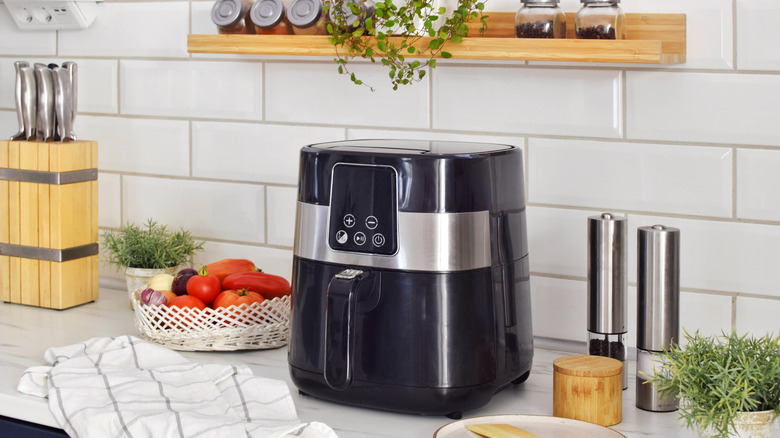 Black air fryer on a kitchen counter with other items surrounding it.
