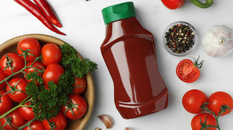 bottle of ketchup surrounded by tomatoes, peppers, herbs, peppercorns, and garlic