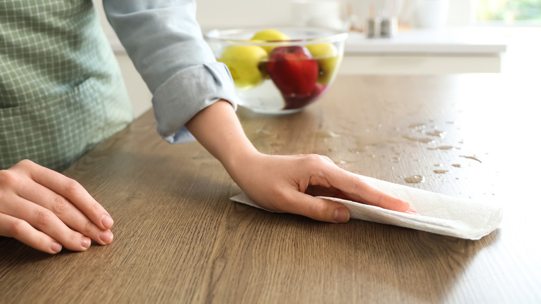 Cleaning up a spill on a wooden table with paper towels