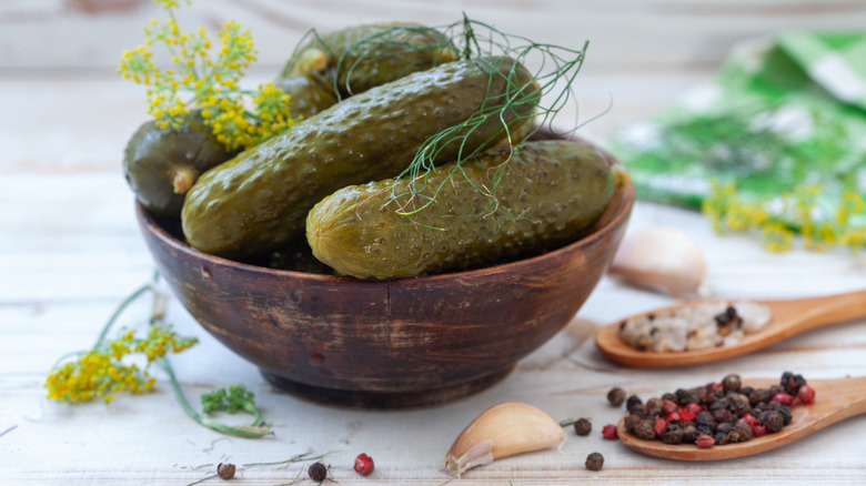 A bowl of pickles next to seasonings and sppons.