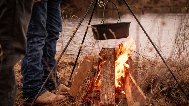 A cowboy is cooking on a cast iron pan over a campfire.