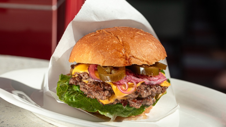 A smashburger with pickled toppings wrapped in paper