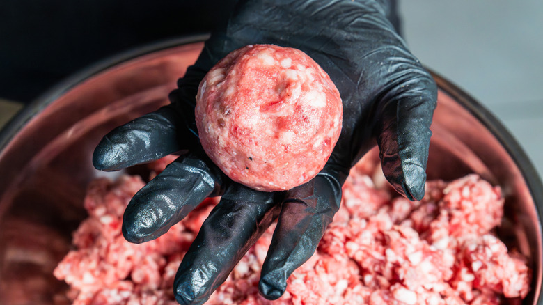 A hand holds a ball of burger meat