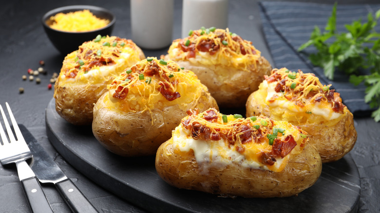 a platter of loaded baked potatoes with cheese, spices, and fresh herbs in the background
