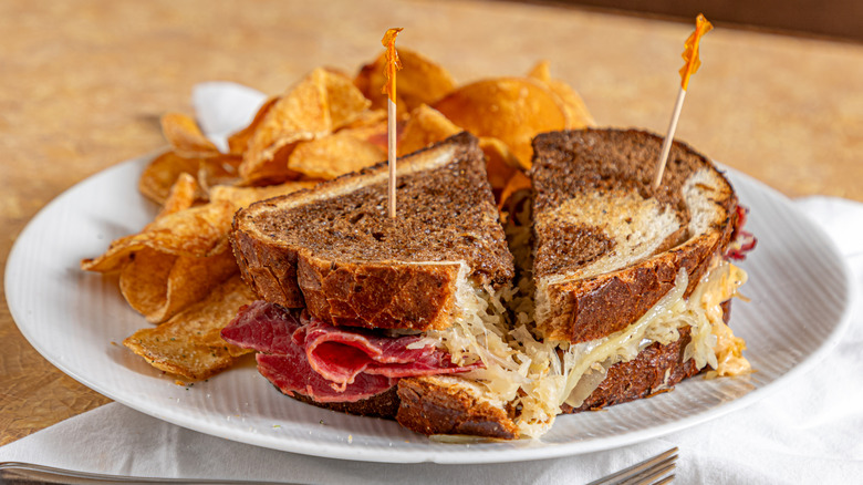 a halved Reuben sandwich on marbled rye bread on a plate with potato chips