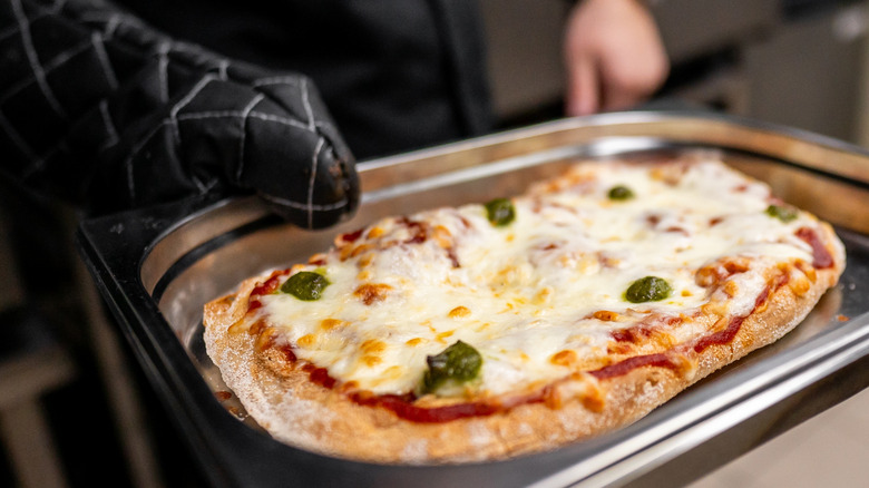 person pulling a jalapeno pizza out of oven