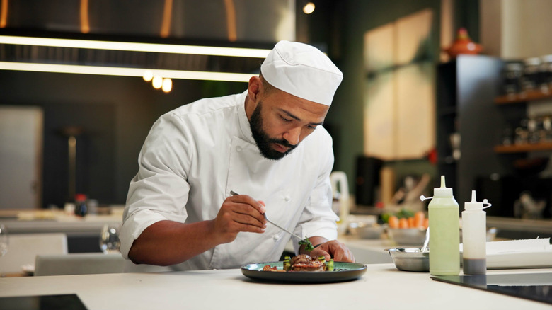 A chef carefully garnishing a dish in an open kitchen
