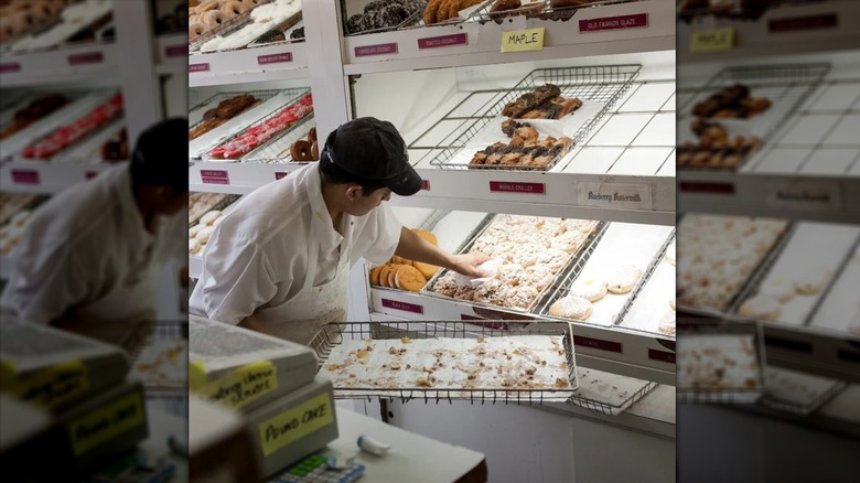 A man replacing a basket of fresh donuts on a donut shelf