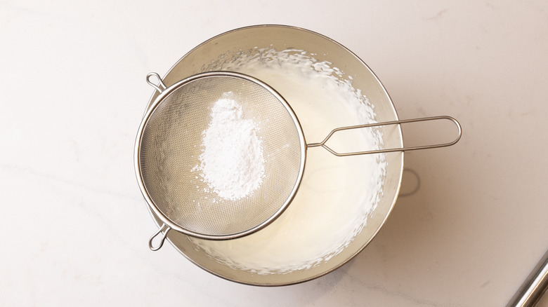 Confectioners' sugar sifting into bowl with whipped cream
