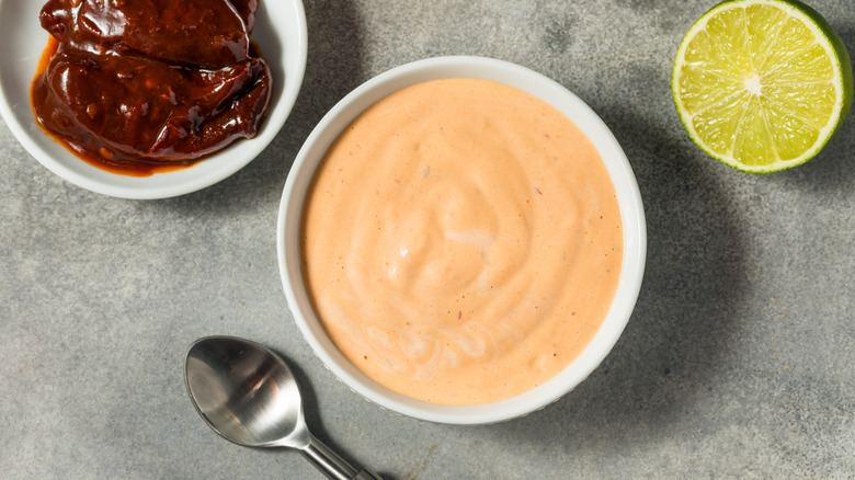 spicy mayo sauce in white bowl with hot sauce and lemon on the side