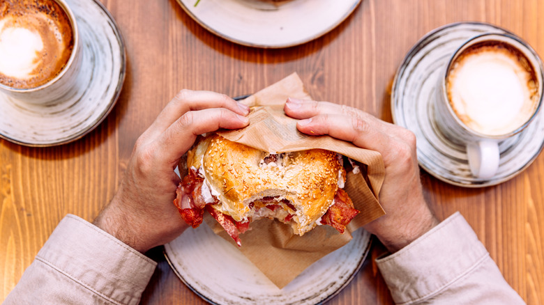 person holding a breakfast sandwich surrounded by lattes