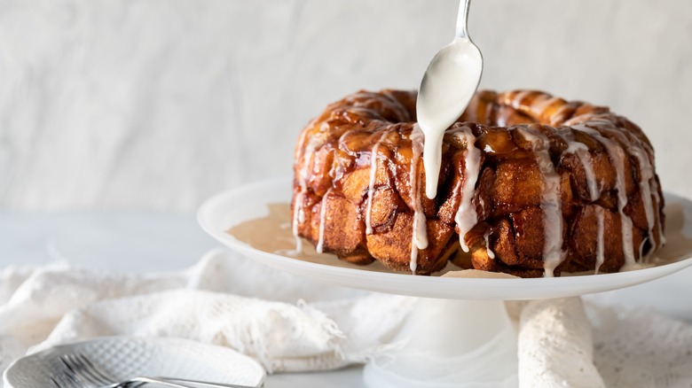 Drizzling glaze on apple cinnamon monkey bread on a cake stand
