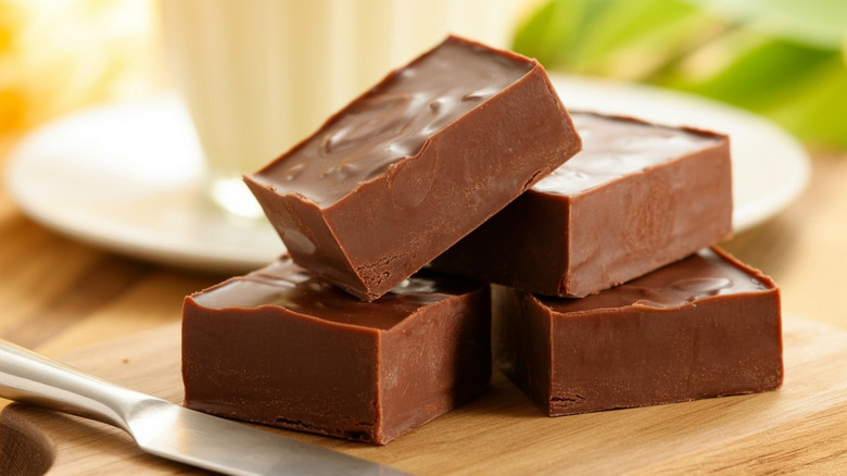 Four pieces of chocolate fudge on a wood board with a cutting knife