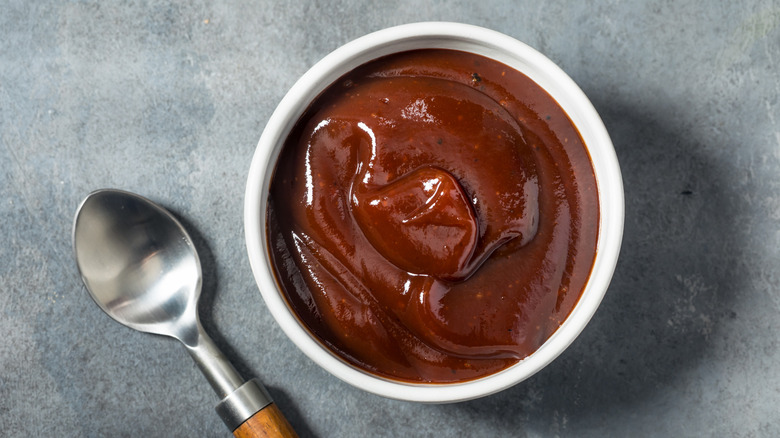 Bowl of barbecue sauce on counter beside a spoon