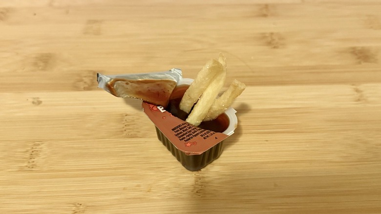 Fries dipped in Popeye's BoldBQ sauce on wooden table