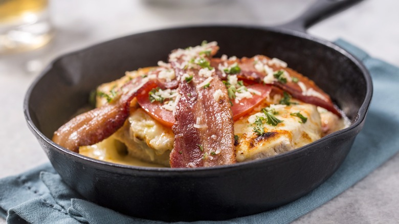 open faced sandwich covered in bacon, tomato, and cheese sauce in a skillet