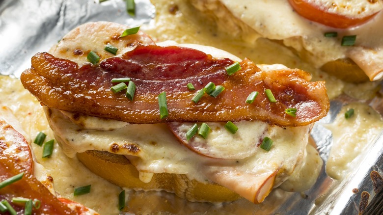 Open-faced sandwich topped with melted cheese, tomato, bacon, and chives