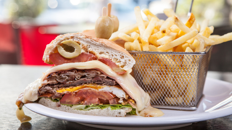 a chivito sandwich piled high with fries alongside
