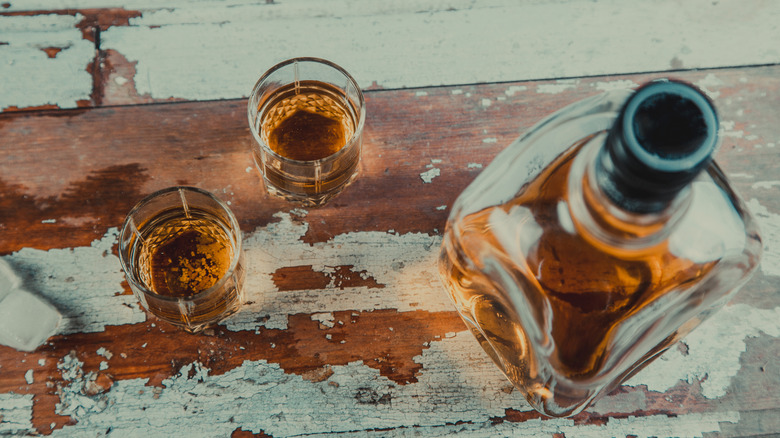 Two shot glasses of whiskey sitting next to a bottle of whiskey on a wood-paneled surface