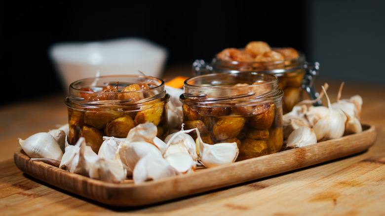 Several jars of garlic confit sit on a tray, surrounded by unpeeled raw garlic cloves