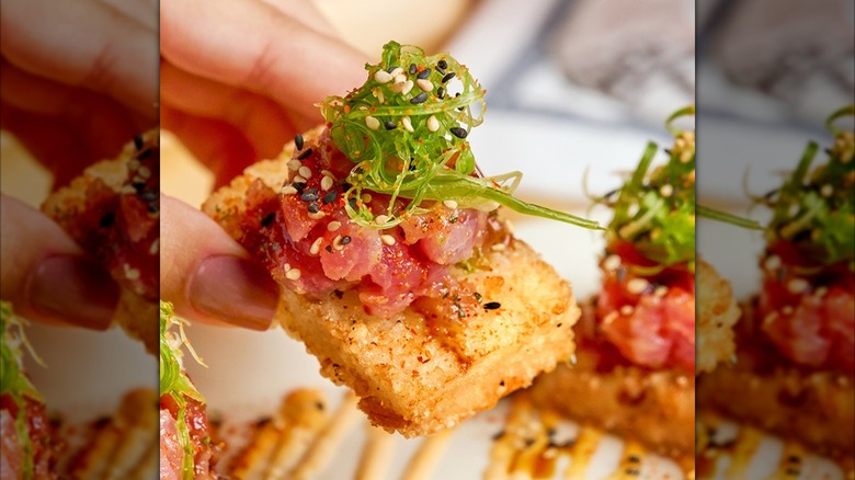 Hand holding piece of the Cheesecake Factory's Spicy Tuna appetizer with green garnish
