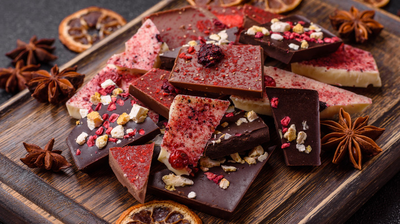 pieces of artisan chocolate bars stacked on a wooden board with spices surrounding them
