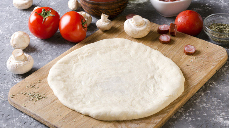 Pizza dough resting on a cutting board, surrounded by fresh ingredients