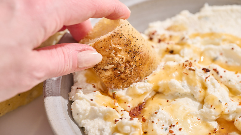 hand dipping bread into cheese dip
