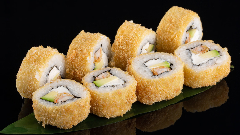 a tempura-fried sushi roll sliced and placed on a leaf against a black background