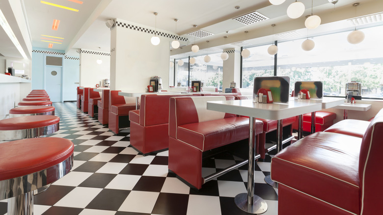 The interior of a modern diner with 1950s style; red stools along a counter and red booths with tables