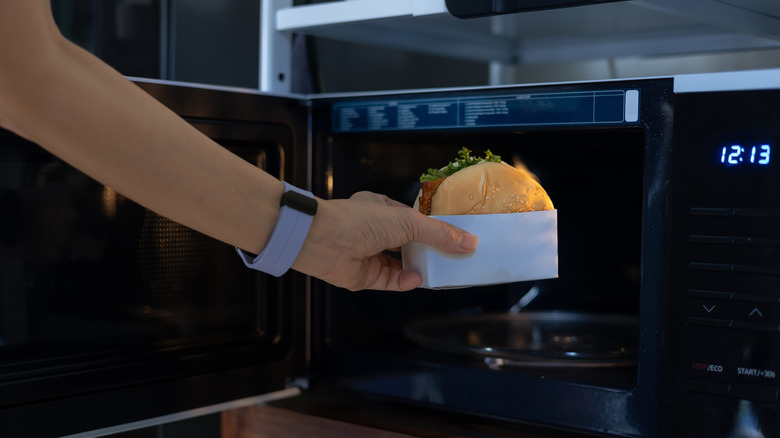 closeup of hand removing burger in sleeve from microwave