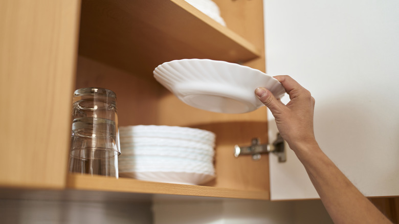Person stacking dishes in kitchen cabinet