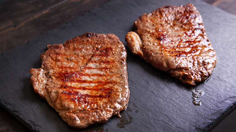 Two cooked beef minute steaks seasoned with black pepper on black board