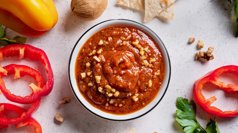 Bowl with bell pepper dip and walnuts next to sliced peppers