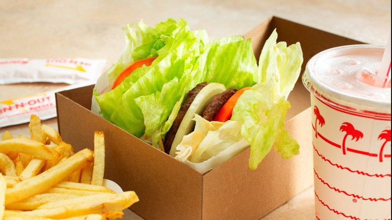 Two In-N-Out style burgers with lettuce wraps in brown cardboard box next to fries and drink cup