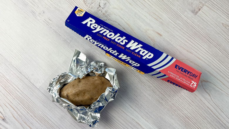a baked potato half-wrapped in aluminum foil beside a roll of Reynolds Wrap aluminum foil
