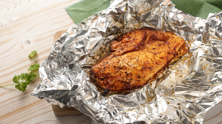 roasted chicken breast in aluminum foil with fresh herbs beside it