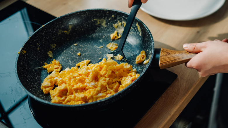 a person cooking scrambled eggs in a nonstick skillet