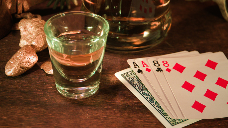 Shot glass full of liquid on a wooden surface with playing cards and gold nuggets