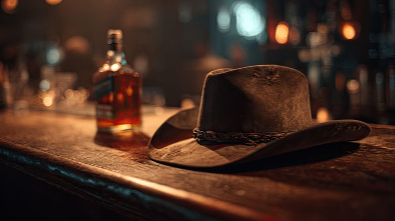 Cowboy hat sitting on a bar beside a bottle of whiskey