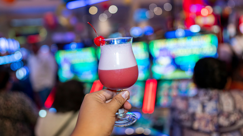 Hand holding cocktail in front of slot machines