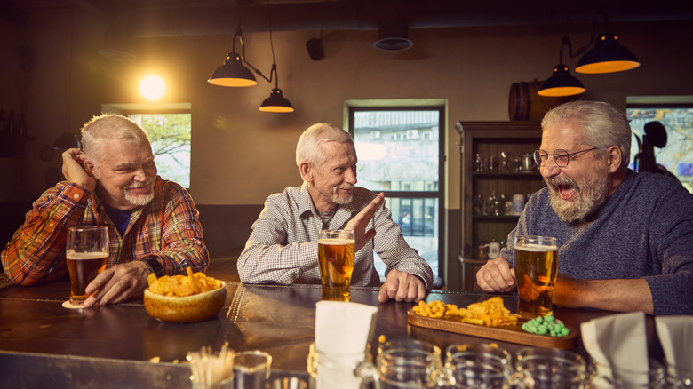 Three older men drinking beer at a pub with snacks