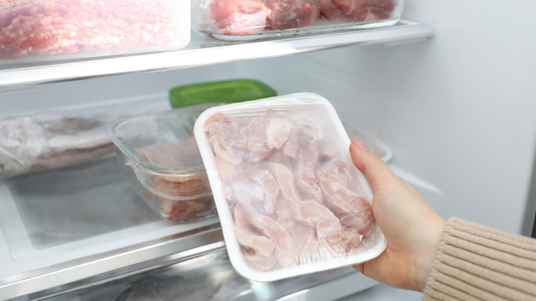 woman placing frozen chicken in fridge